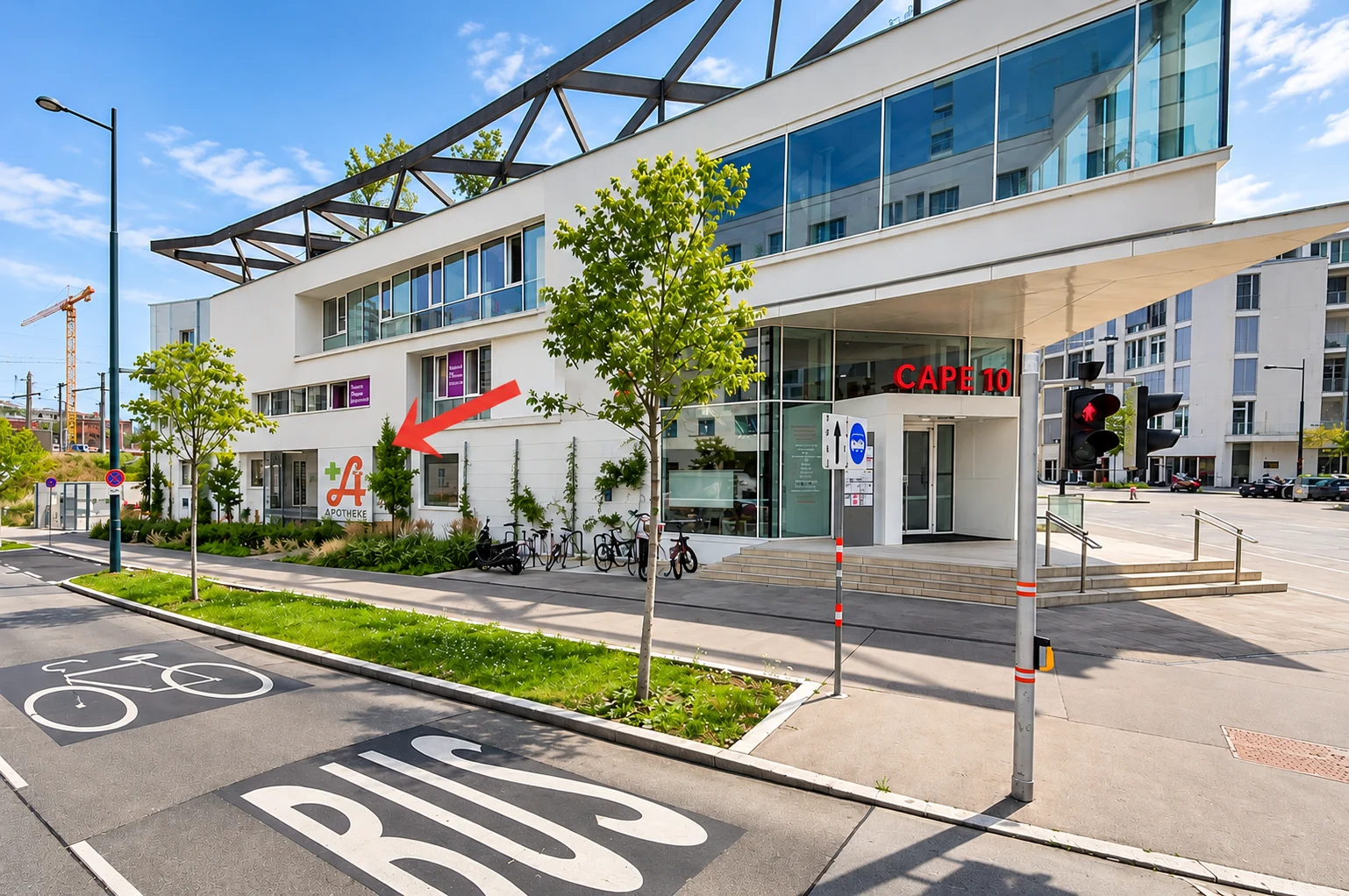 Das Gebäude CAPE 10 von der Straße aus. Ein roter Pfeil zeigt links vom Haupteingang auf das Fenster der Nachtdienstausgabe beim Apothekentransparent.